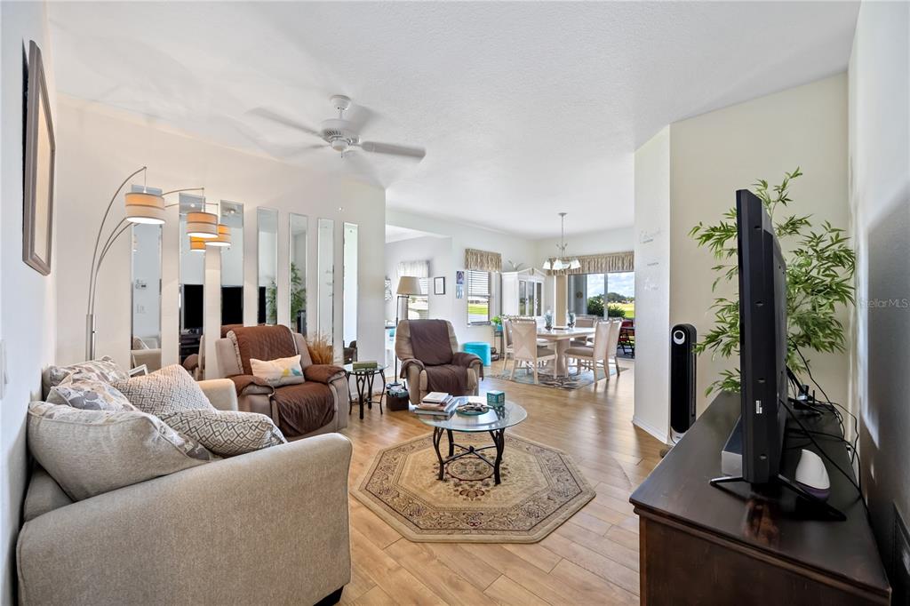 A living room with light wood flooring, a glass coffee table, and a dining area beyond — 5800 SABAL TRACE DRIVE UNIT 301, NORTH PORT, FL