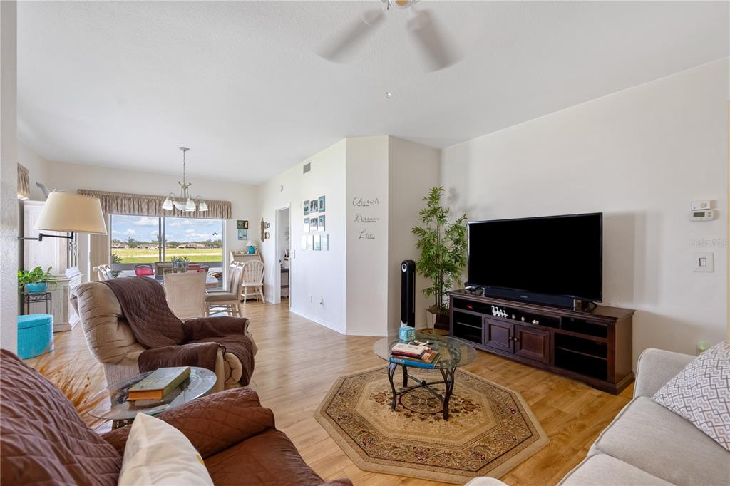 A living room with wood-look flooring, a television console, and an adjacent dining area — 5800 SABAL TRACE DRIVE UNIT 301, NORTH PORT, FL