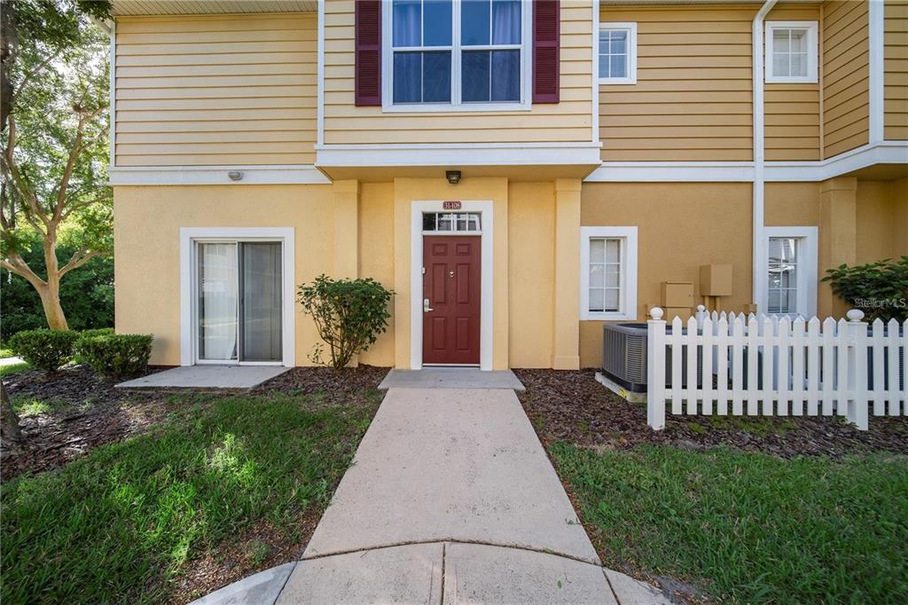 A tan two-story townhouse exterior features a red front door and a white picket fence — 2601 GALA ROAD S UNIT 31-108, KISSIMMEE, FL