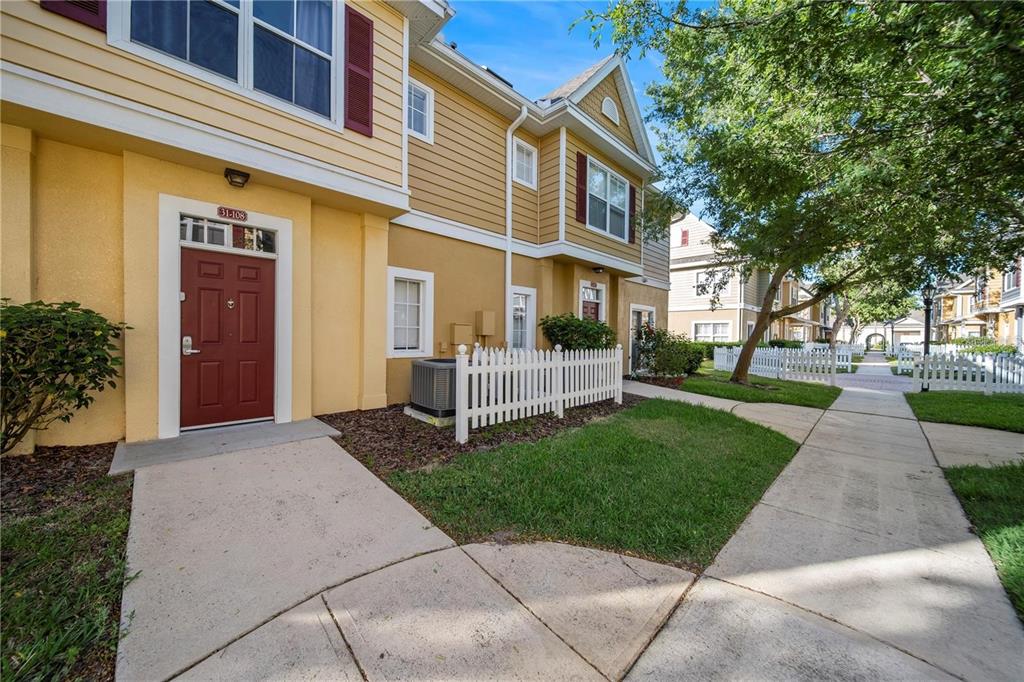 A yellow two-story townhouse with a red front door and a white picket fence — 2601 GALA ROAD S UNIT 31-108, KISSIMMEE, FL