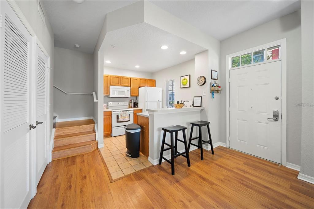 A kitchen with wood cabinets and a breakfast bar opens to an entryway with stairs — 2601 GALA ROAD S UNIT 31-108, KISSIMMEE, FL