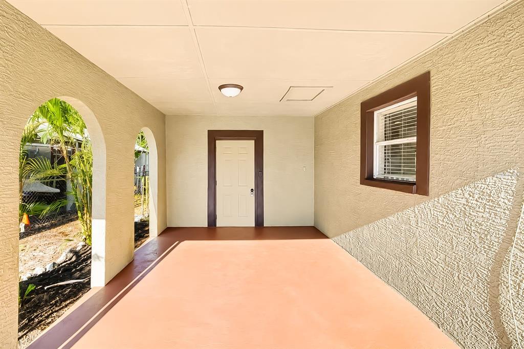 A covered patio features a painted concrete floor, arched openings, a white door, and stucco walls — 4219 35TH STREET W, BRADENTON, FL