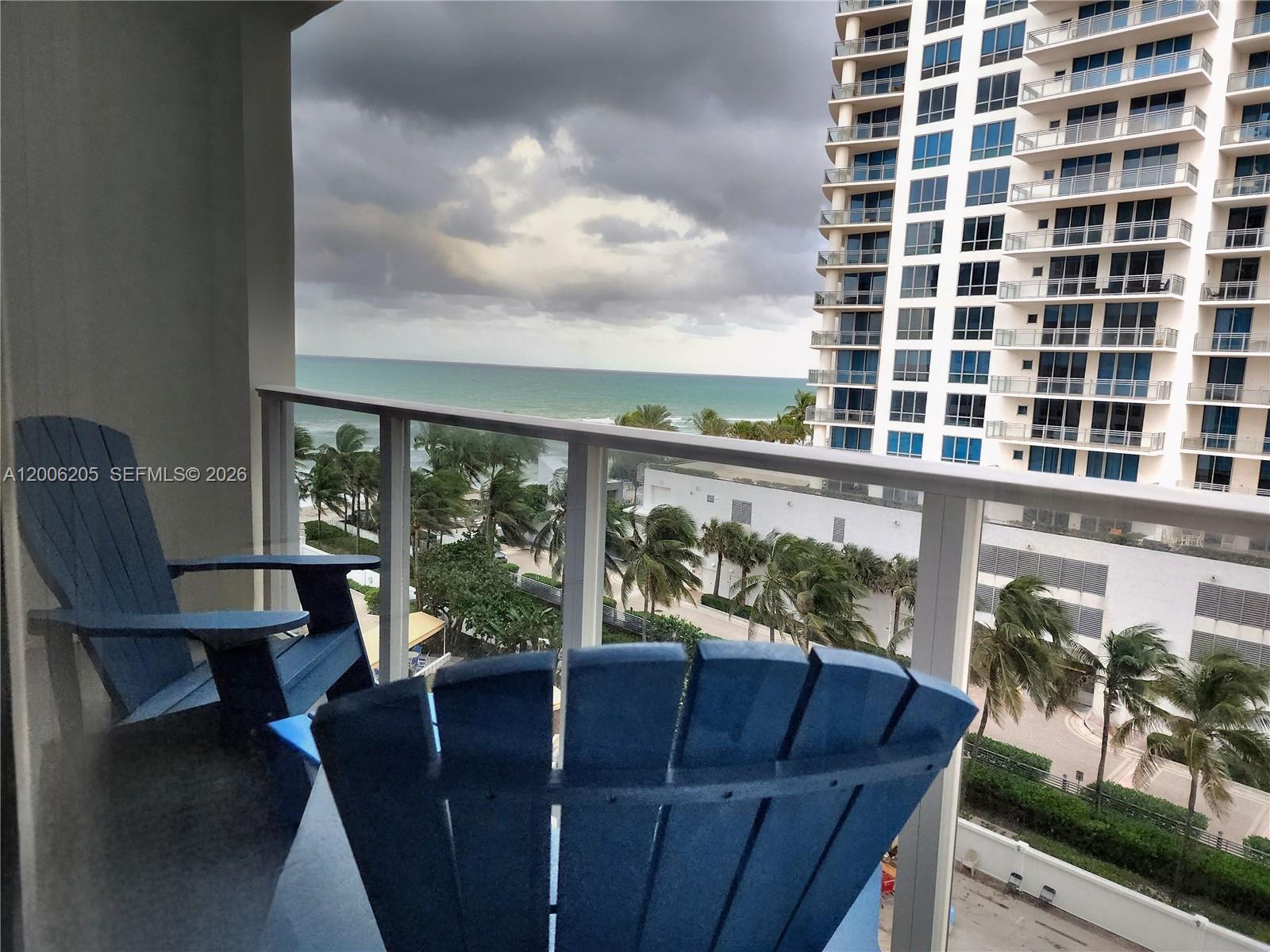 A balcony with two blue Adirondack chairs overlooks the ocean and a high-rise building — 3505 S Ocean Dr # 719, Hollywood FL 33019, HOLLYWOOD, FL