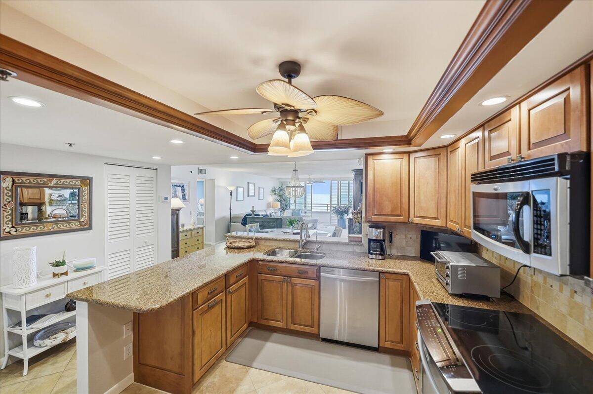 A kitchen with wood cabinets, granite countertops, and stainless steel appliances opens to a living area — 9950 S Ocean Drive # 604, Jensen Beach FL 34957, JENSEN BEACH, FL