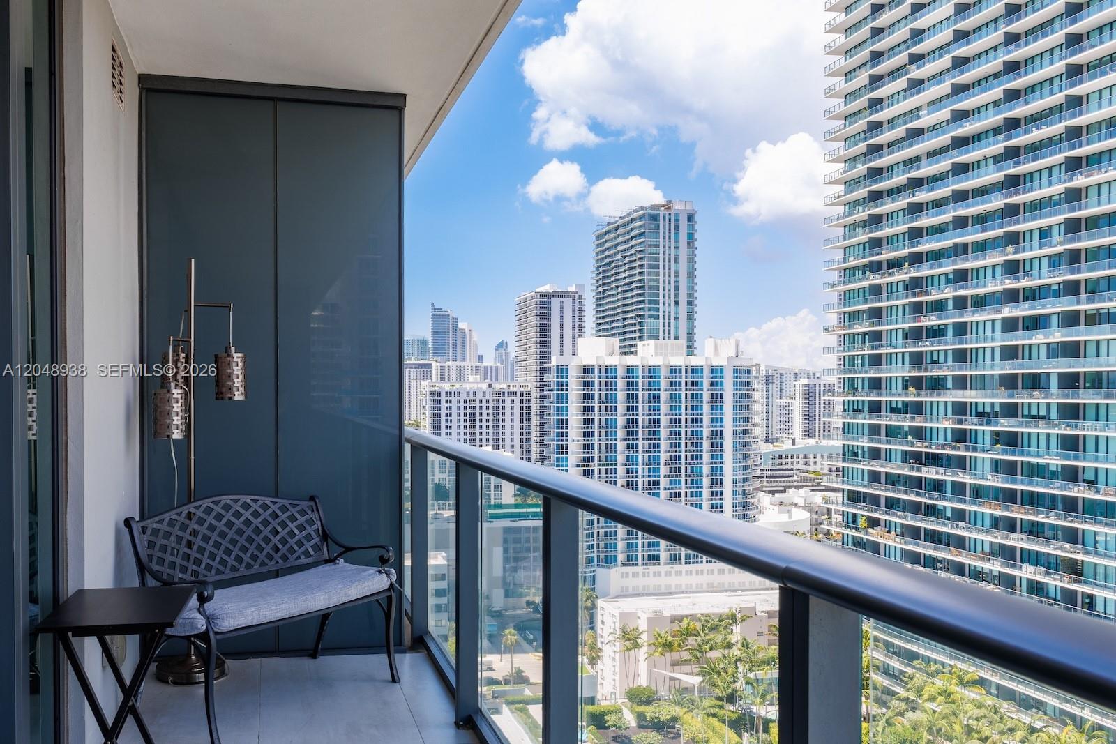 A balcony with a metal bench and floor lamp overlooks a dense city skyline — 3131 NE 7th Ave # 2003, Miami FL 33137, MIAMI, FL