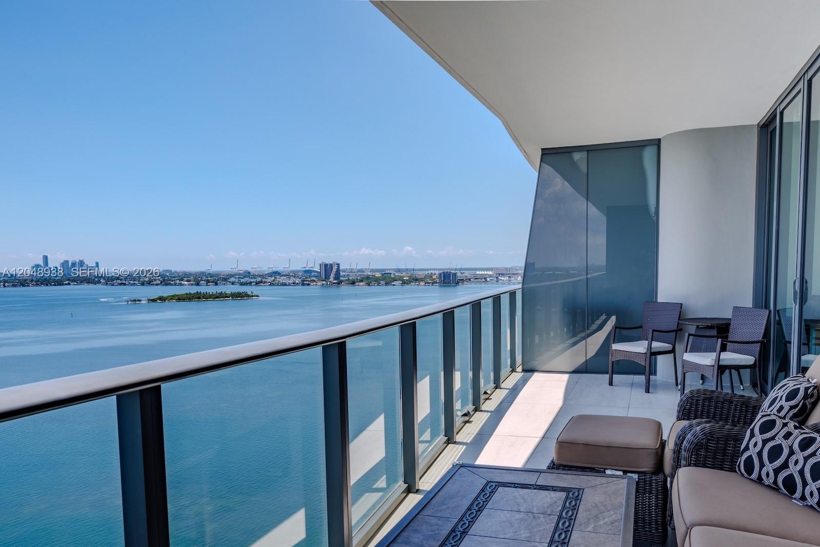 A balcony with glass railings overlooks a bay with a distant city skyline — 3131 NE 7th Ave # 2003, Miami FL 33137, MIAMI, FL