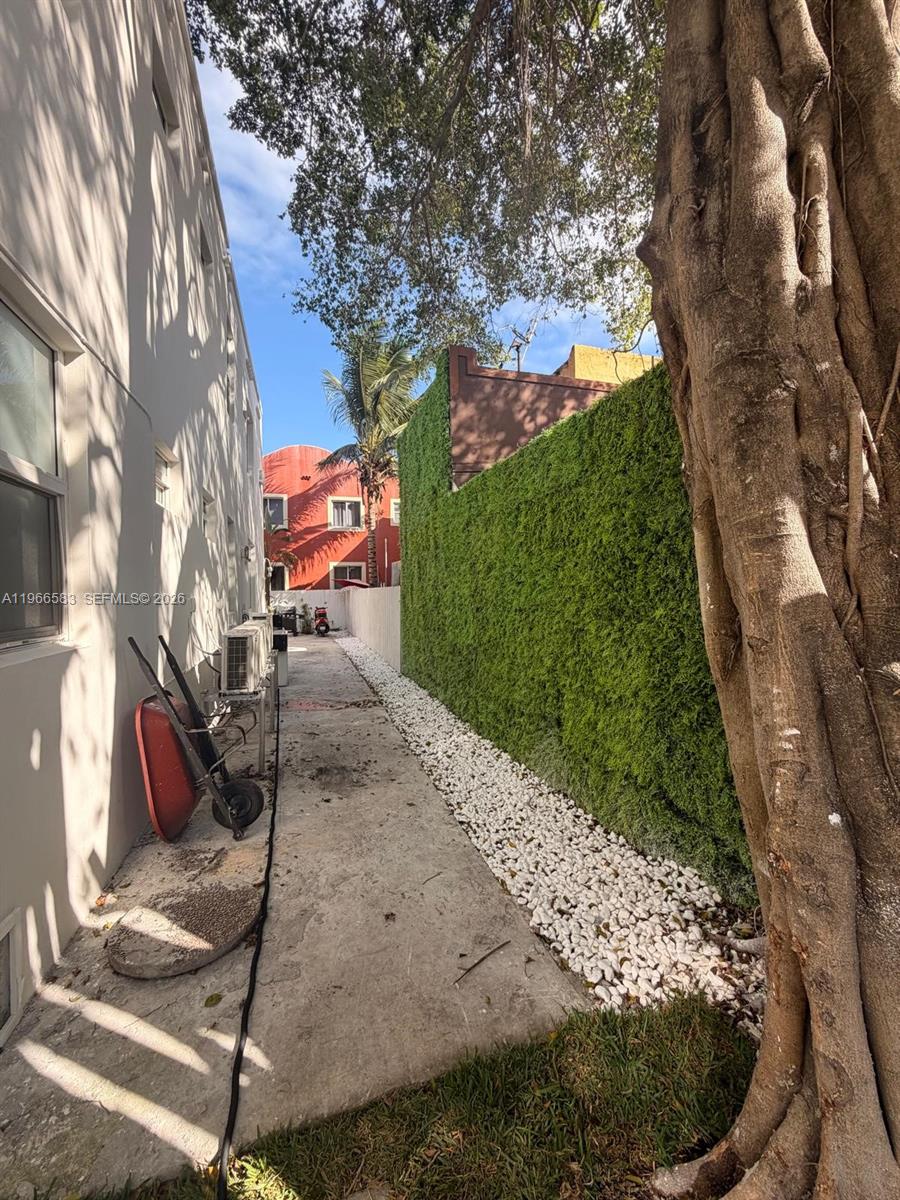 A narrow concrete walkway runs between a building wall and a tall green hedge — 337 SW 10th Ave, Miami FL 33130, MIAMI, FL