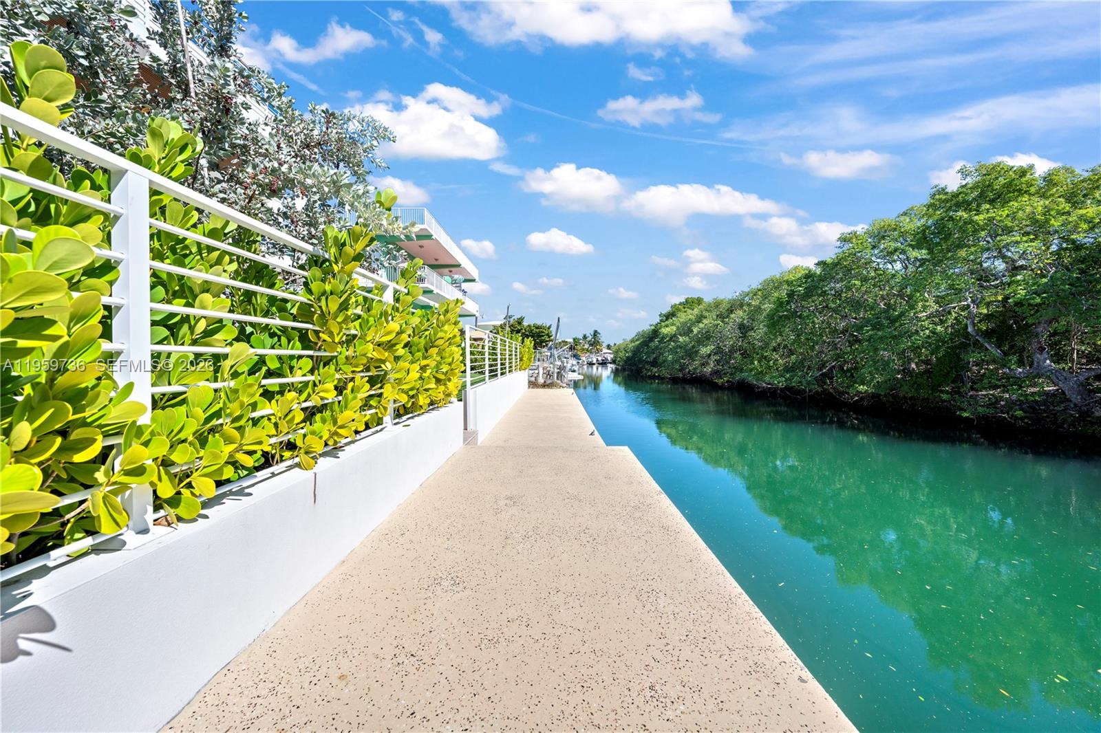 A concrete walkway runs alongside a canal bordered by lush green trees and a fence — 124 Orchid St, Plantation Key FL 33070, PLANTATION KEY, FL