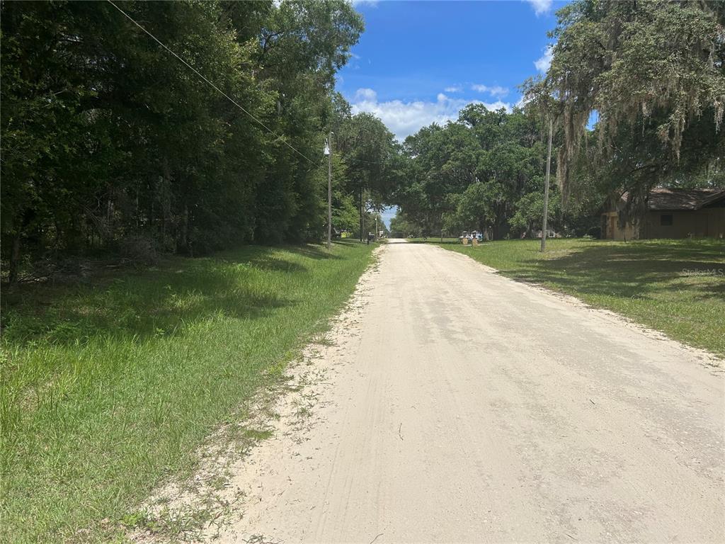 A dirt road runs through a wooded residential area under a blue sky — SW 111 LANE, DUNNELLON, FL