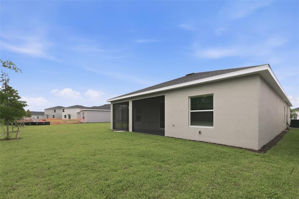 The exterior rear view of a single-story house features a screened-in porch and lawn — 26639 WILGROVE PLACE, PUNTA GORDA, FL