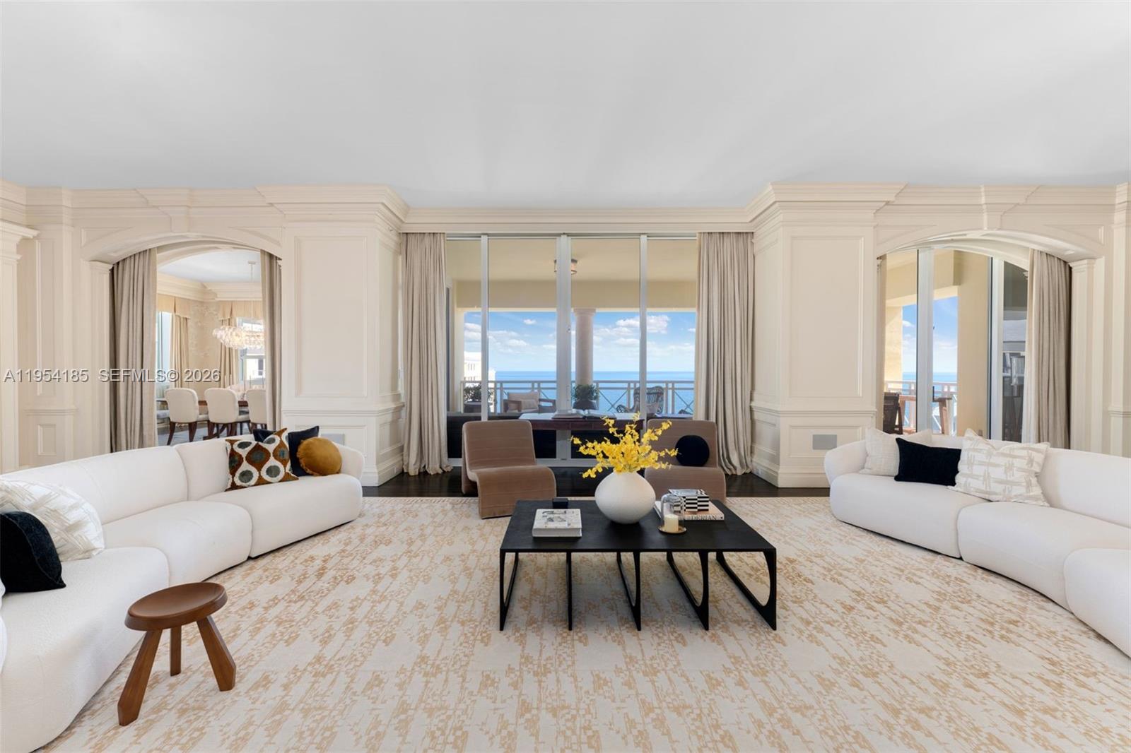 A bright living room features two white curved sofas, a black coffee table, and ocean views — 445 Grand Bay Drive # 1A, Key Biscayne FL 33149, KEY BISCAYNE, FL