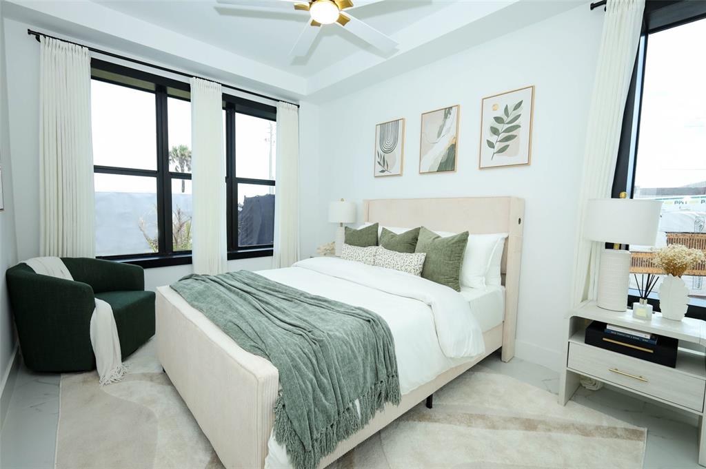 A modern bedroom features a queen bed, green accent pillows, a side chair, and large windows — 2360 OCEAN SHORE BOULEVARD UNIT 20, ORMOND BEACH, FL