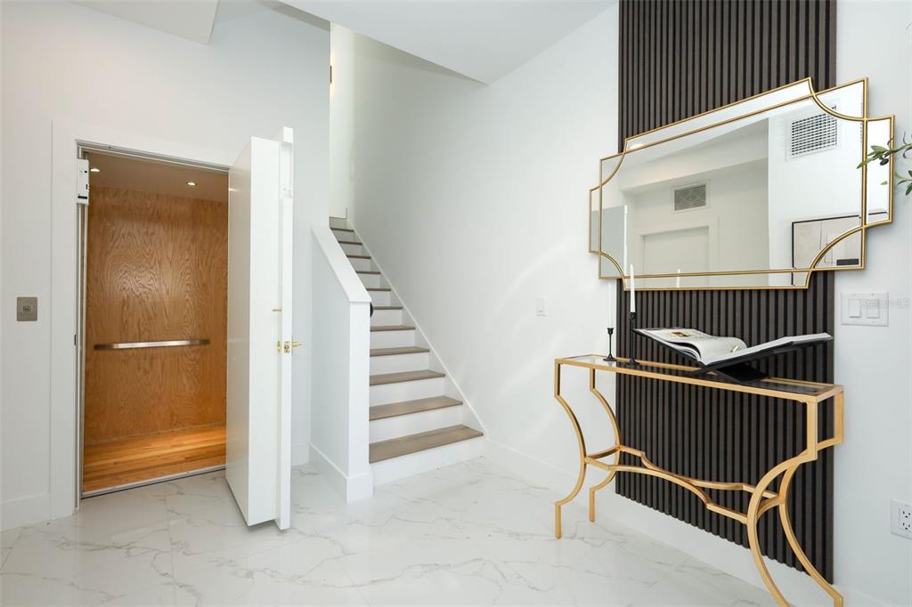 A modern entryway features a white staircase, a wood-paneled elevator, and a gold console table — 2360 OCEAN SHORE BOULEVARD UNIT 20, ORMOND BEACH, FL
