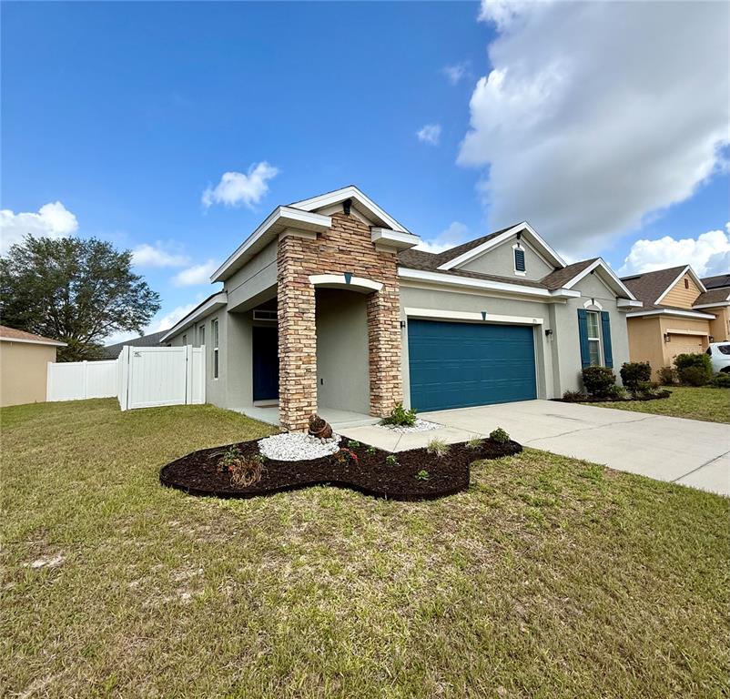 A single-story house with a stone-accented entryway, blue garage door, and a white fence — 173 TRACY CIRCLE, HAINES CITY, FL
