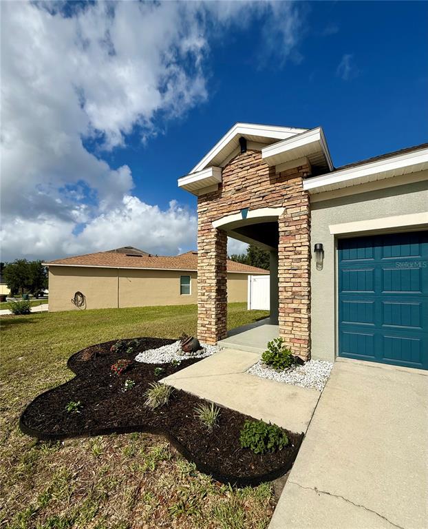 A stone-accented entryway leads to a house with a blue garage door and landscaping — 173 TRACY CIRCLE, HAINES CITY, FL