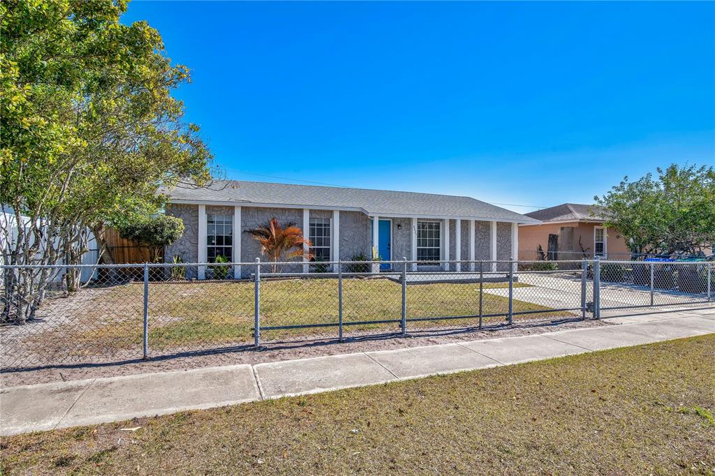 A single-story house with a gray stone facade and a chain-link fence in front — 4027 GANDER AVENUE, ORLANDO, FL