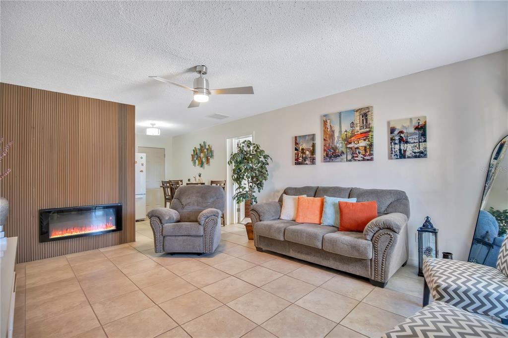 A living room features a fireplace with a wood-slat wall, tile flooring, and gray furniture — 4027 GANDER AVENUE, ORLANDO, FL