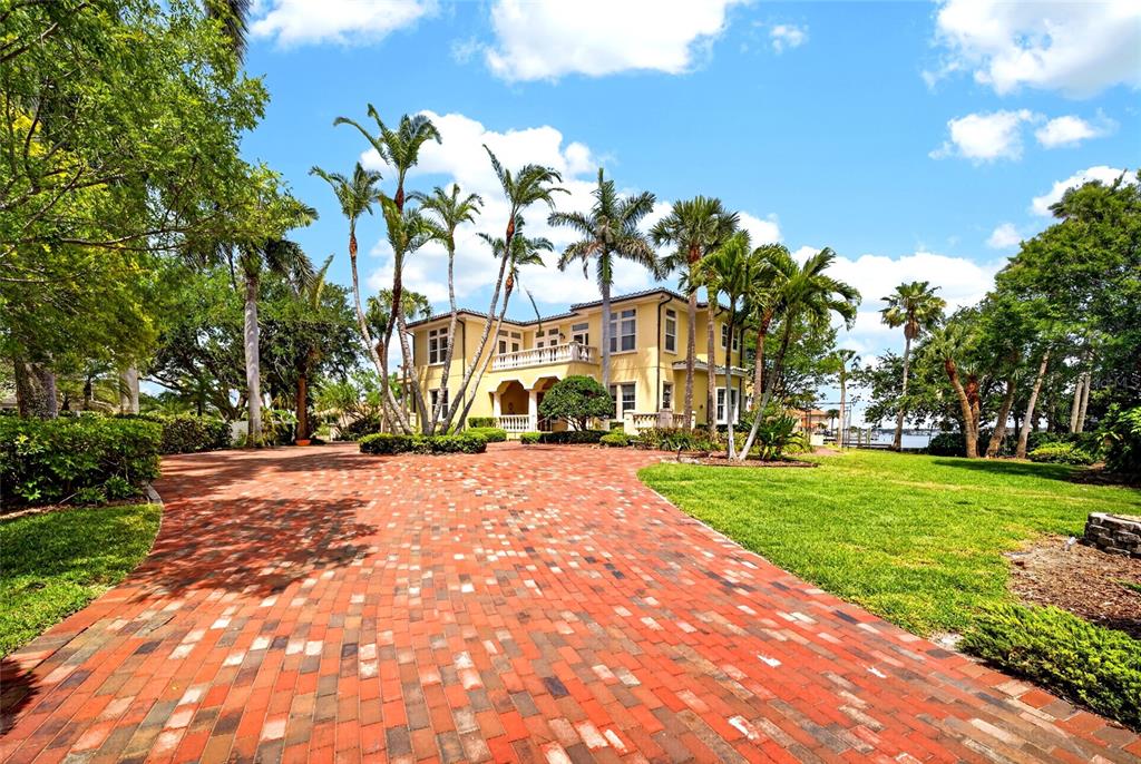 A two-story yellow house with a brick driveway and palm trees under a blue sky — 115 18TH STREET, BELLEAIR BEACH, FL