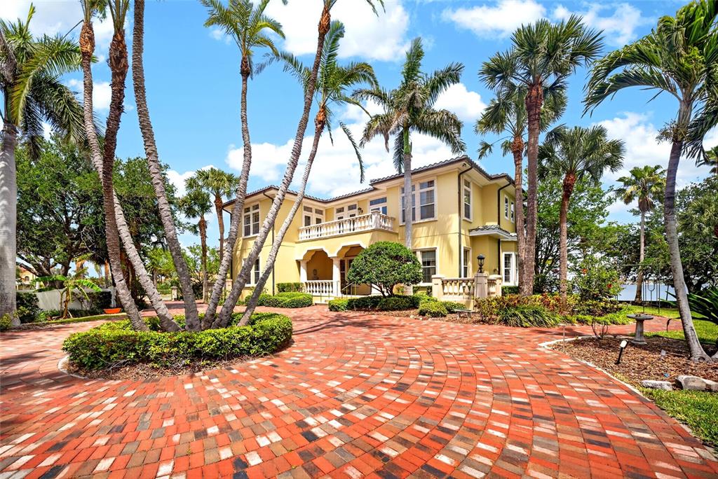 A yellow two-story house with a brick driveway and palm trees under a blue sky — 115 18TH STREET, BELLEAIR BEACH, FL