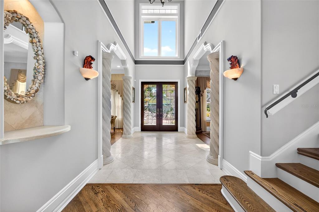 A grand foyer features a high ceiling, spiral columns, tile flooring, and a wooden staircase — 115 18TH STREET, BELLEAIR BEACH, FL