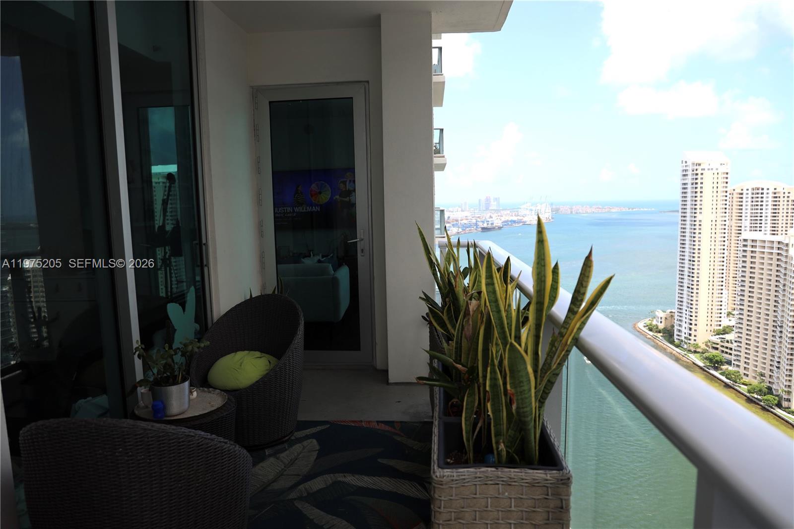 A balcony features wicker chairs, potted snake plants, and a view of the ocean — 300 S Biscayne Blvd # 3504, Miami FL 33131, MIAMI, FL