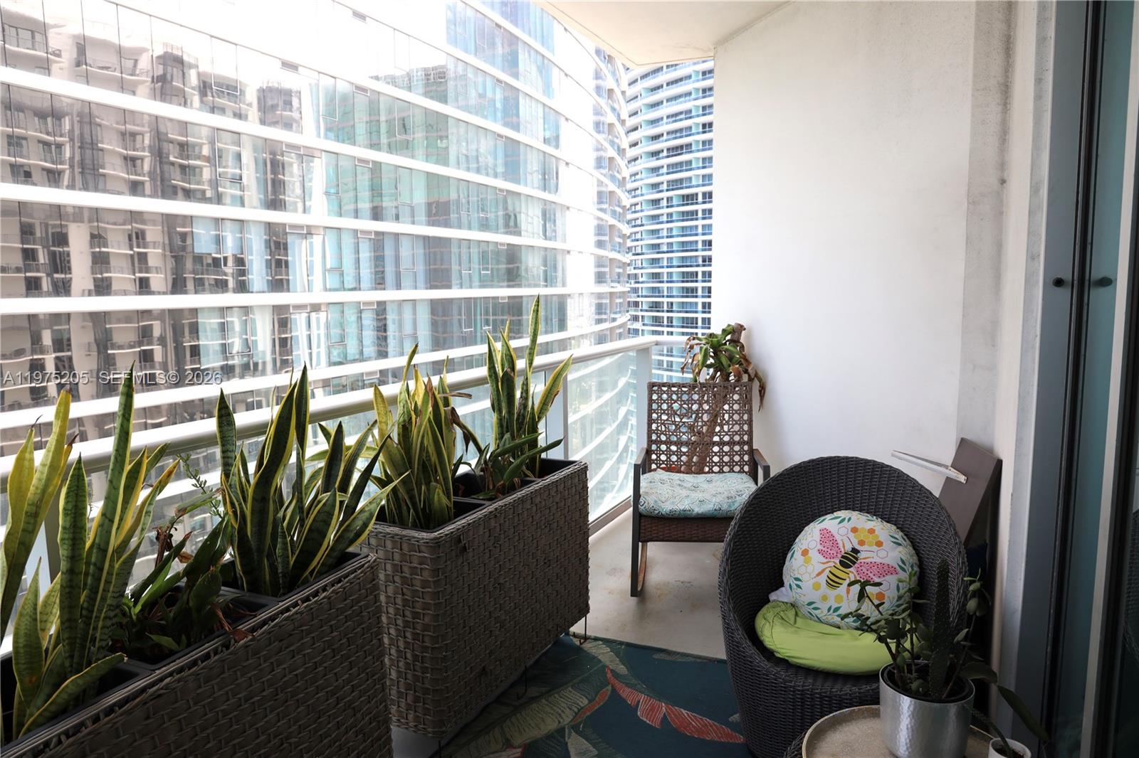 A balcony features two large wicker planters with snake plants, two chairs, and city views — 300 S Biscayne Blvd # 3504, Miami FL 33131, MIAMI, FL