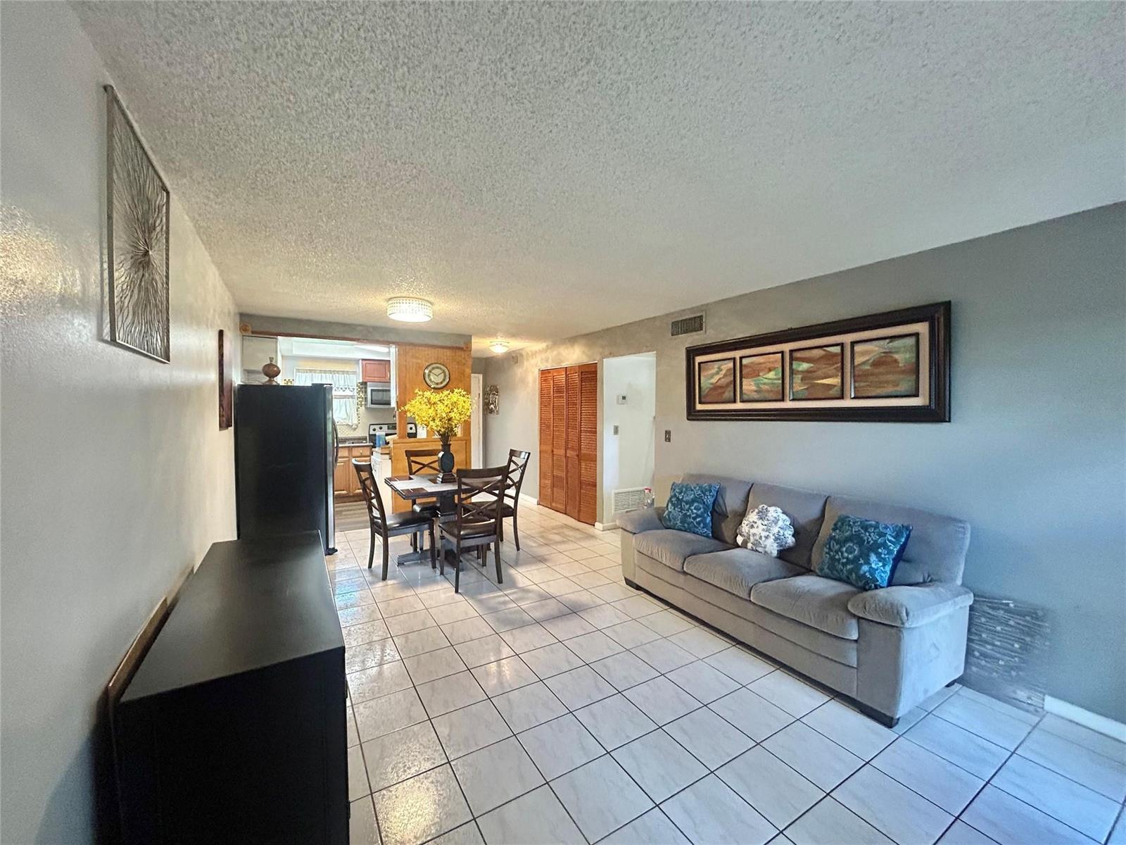 A living and dining area features white tile floors, a gray sofa, and wood-paneled closets — 6100 Forest Hill Boulevard # 101, West Palm Beach FL 33415, WEST PALM BEACH, FL