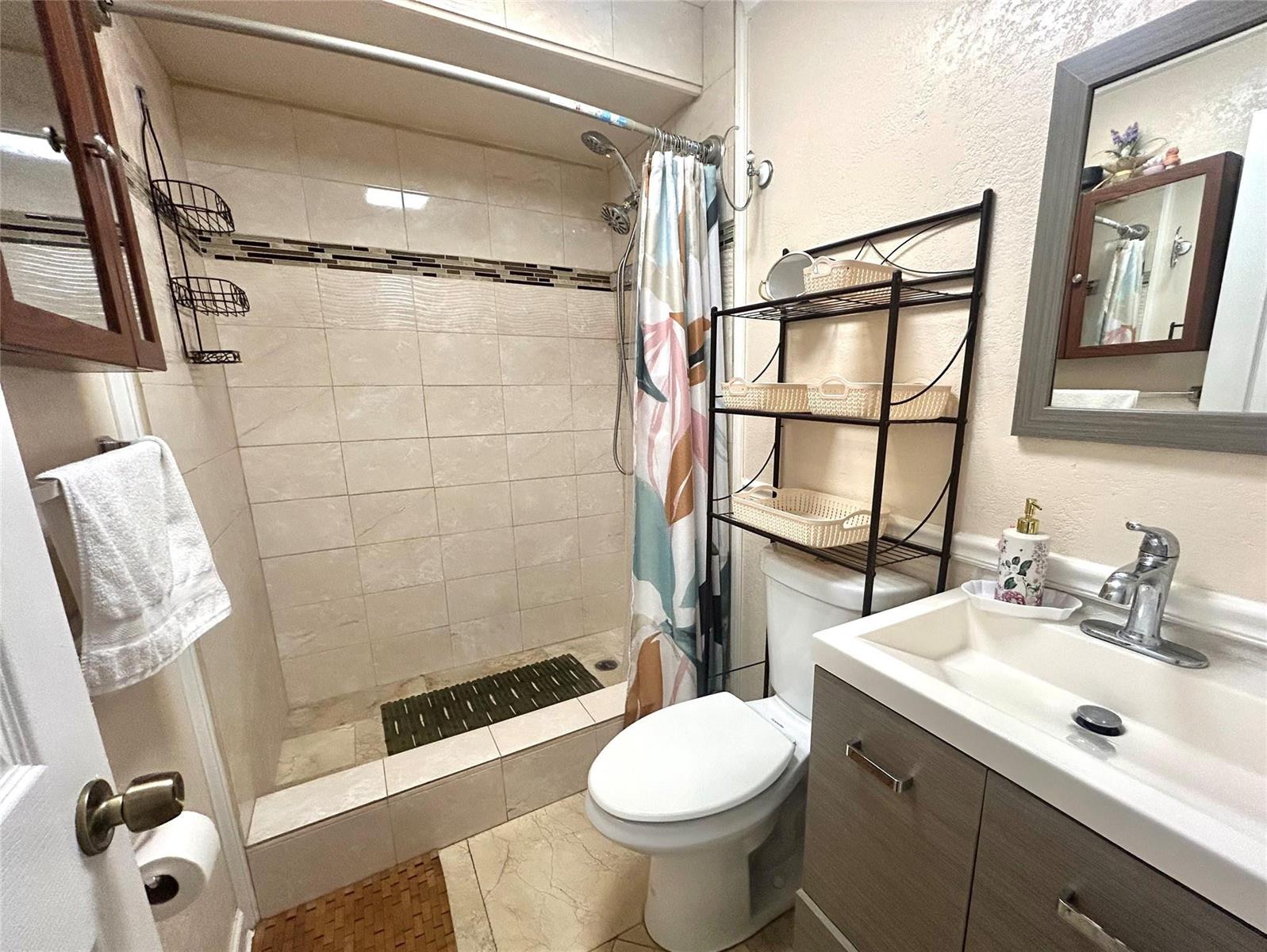 A bathroom features a tiled walk-in shower, a toilet with an over-the-toilet rack, and a vanity — 6100 Forest Hill Boulevard # 101, West Palm Beach FL 33415, WEST PALM BEACH, FL