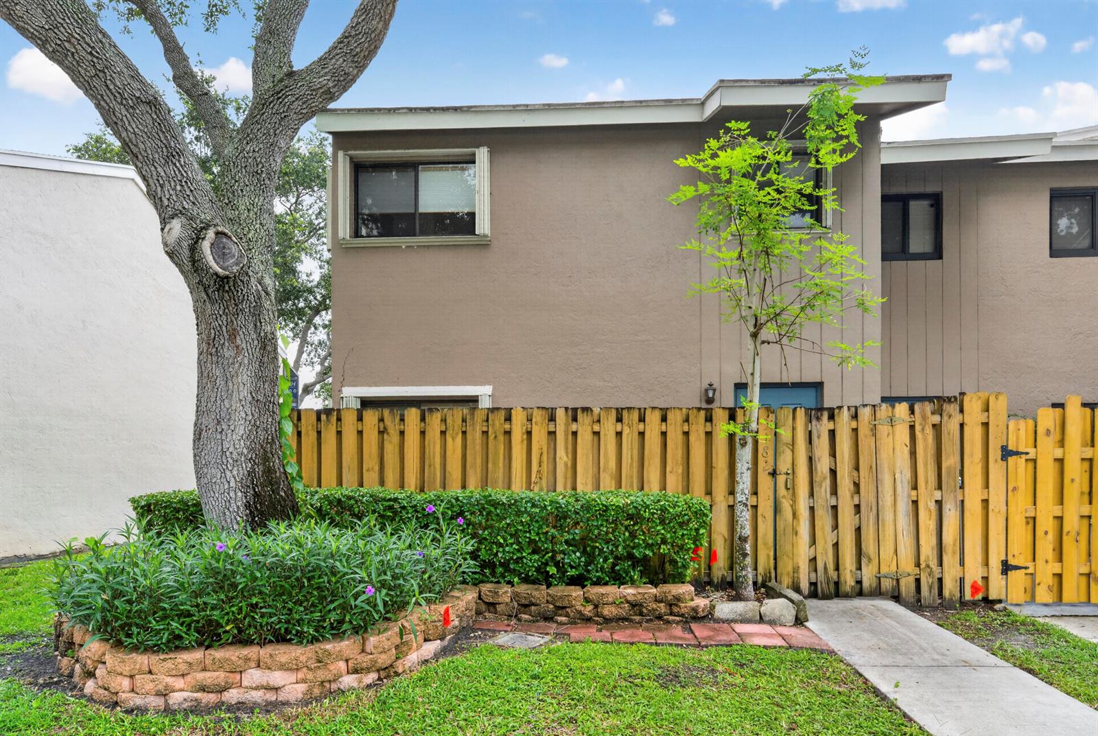 A two-story brown townhouse features a wooden fence, a brick planter, and a large tree — 5182 S University Drive, Davie FL 33328, DAVIE, FL