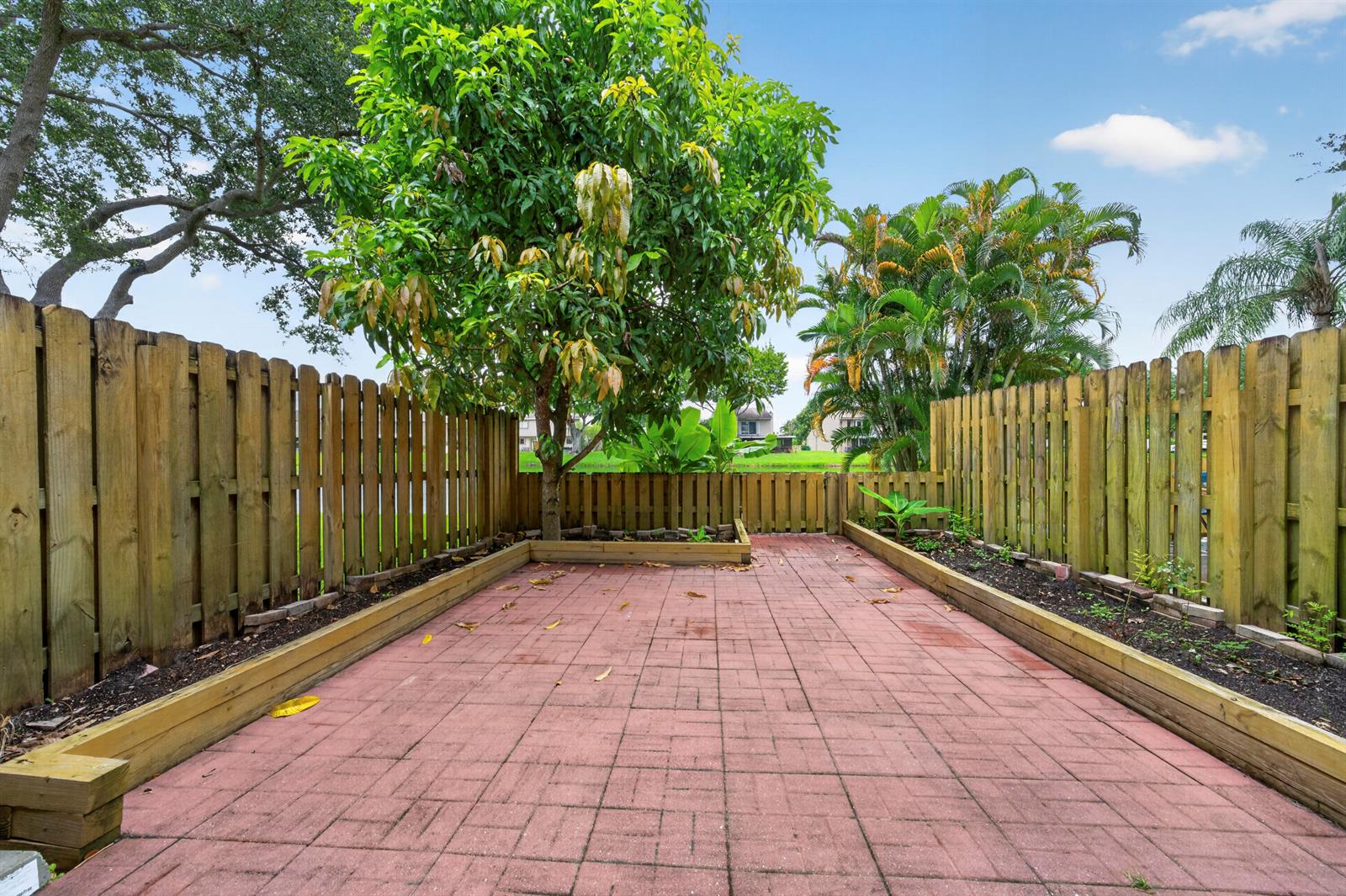 A backyard patio features red pavers, raised garden beds, and a wooden fence — 5182 S University Drive, Davie FL 33328, DAVIE, FL