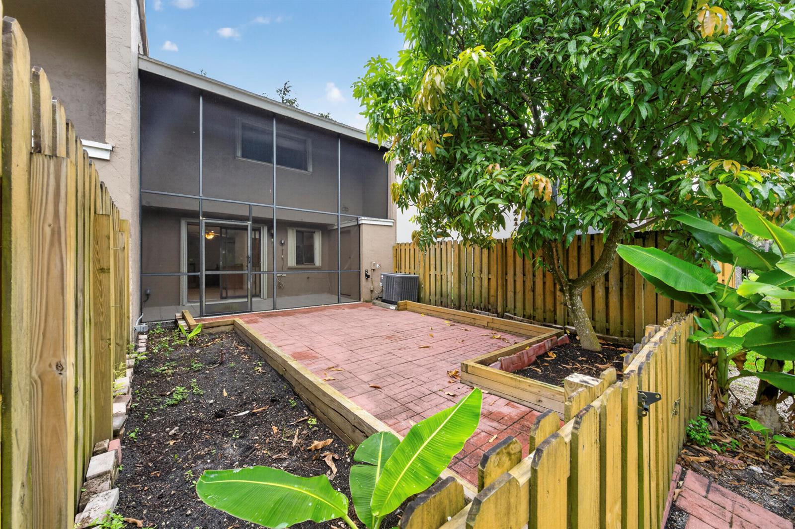 A fenced backyard features a brick patio, a screened-in porch, and a large tree — 5182 S University Drive, Davie FL 33328, DAVIE, FL