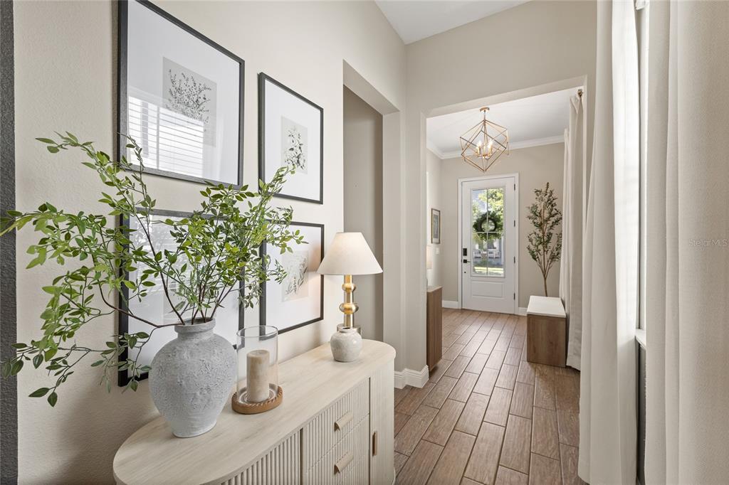 A bright entryway features a light wood console table, framed wall art, and tile flooring — 9542 REYMONT STREET, ORLANDO, FL