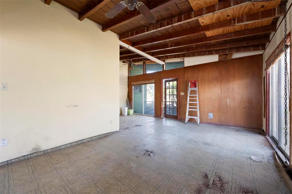 A sunroom features exposed wood ceiling beams, wood-paneled walls, tile flooring, and a step ladder — 2956 GREENBRIAR STREET, SARASOTA, FL