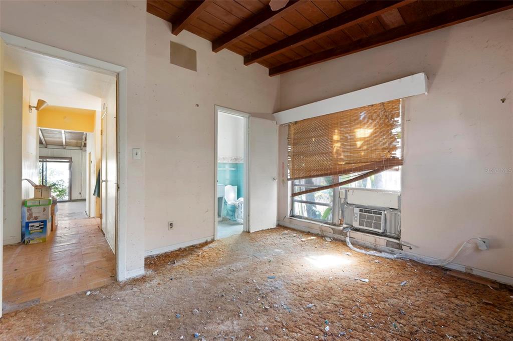 A bedroom with a wood-beamed ceiling, worn carpet, and a window air conditioning unit — 2956 GREENBRIAR STREET, SARASOTA, FL