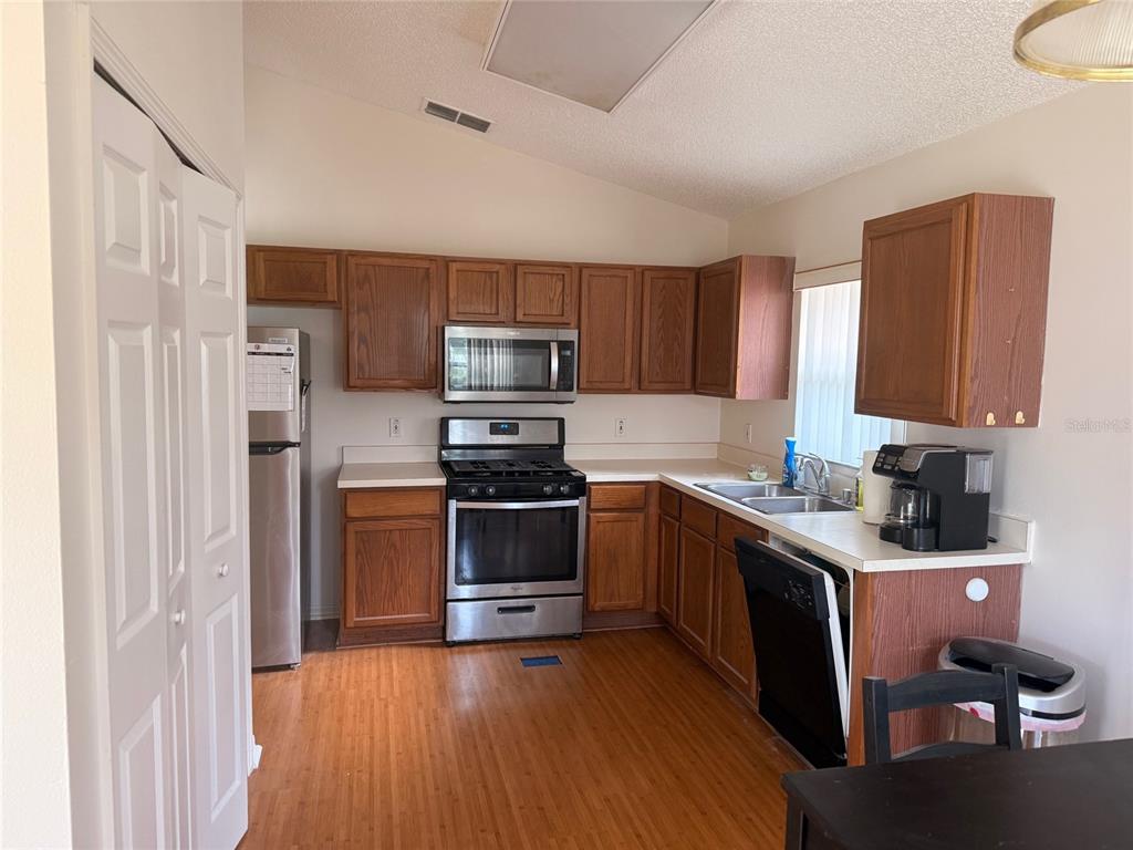 A kitchen features wood cabinets, stainless steel appliances, and light-colored countertops over wood-look flooring — 610 TUTEN TRAIL, ORLANDO, FL
