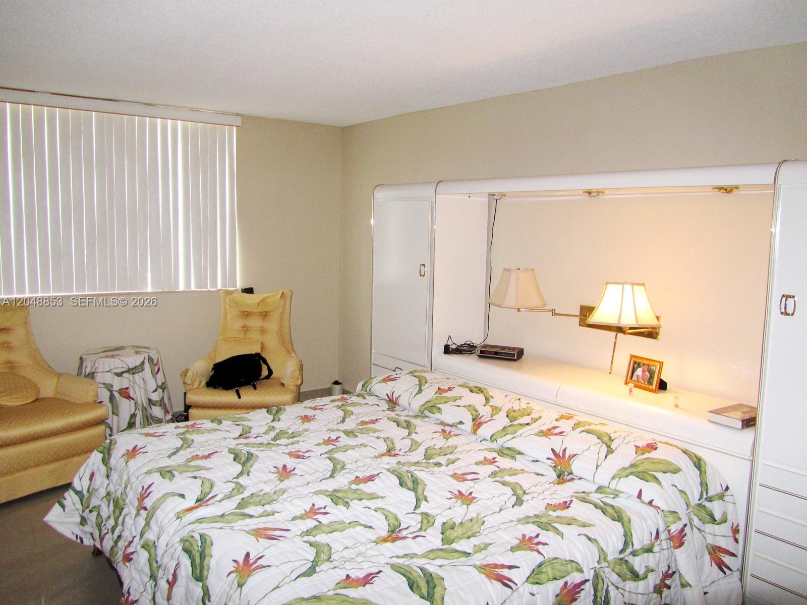 A bedroom features a floral bedspread, two yellow armchairs, and a white built-in headboard — 1833 S Ocean Dr # 911, Hallandale Beach FL 33009, HALLANDALE BEACH, FL