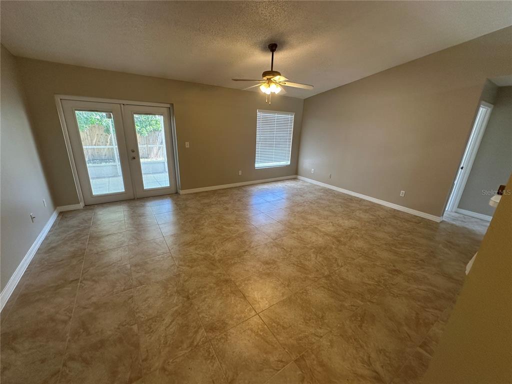 An empty room features tan tile flooring, a ceiling fan, French doors, and a window — 660 MARLENE DRIVE, OCOEE, FL