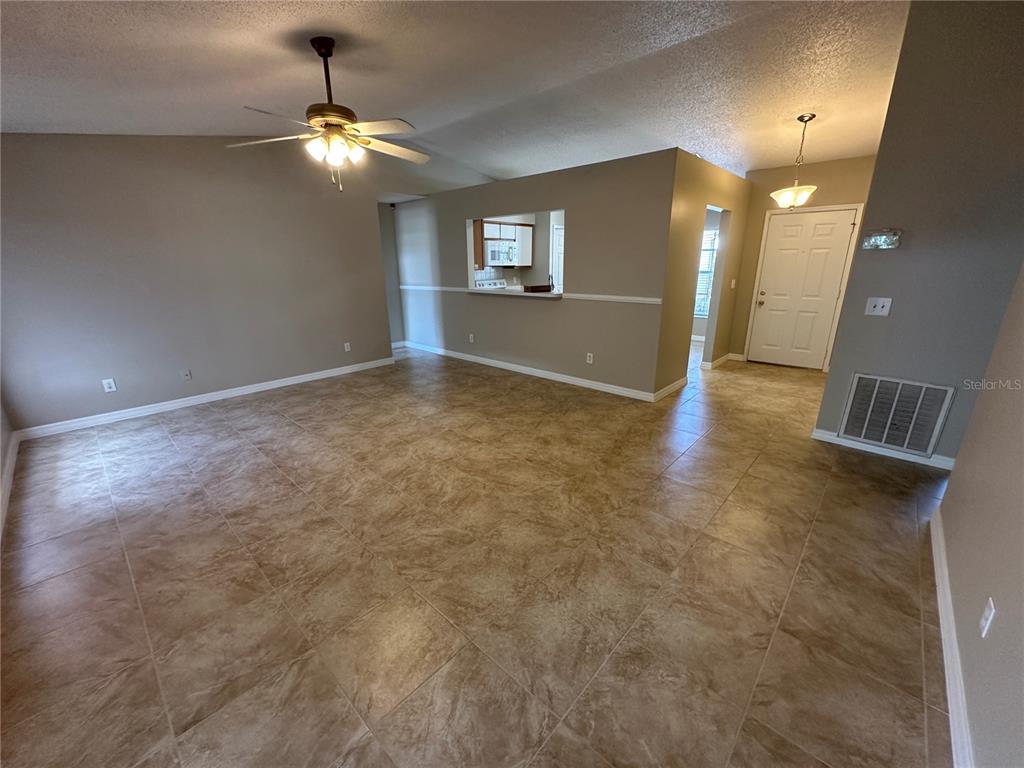A living room with tan walls, tile flooring, a ceiling fan, and a kitchen pass-through — 660 MARLENE DRIVE, OCOEE, FL