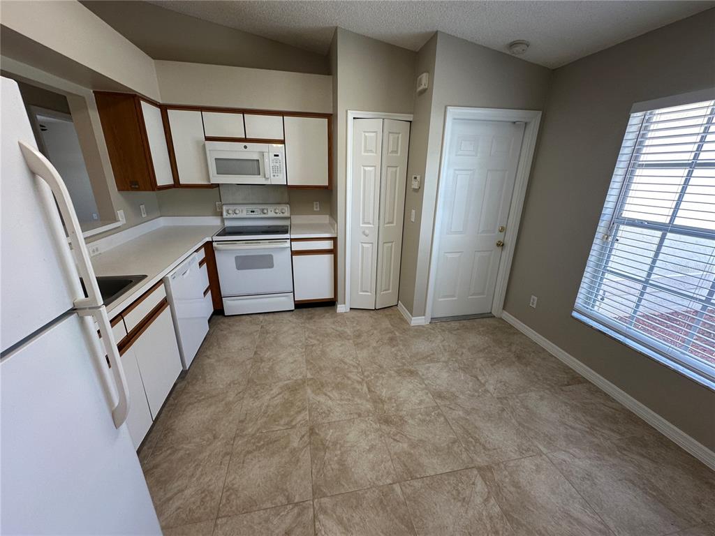 A kitchen features white cabinets, white appliances, beige tile flooring, and a window with blinds — 660 MARLENE DRIVE, OCOEE, FL