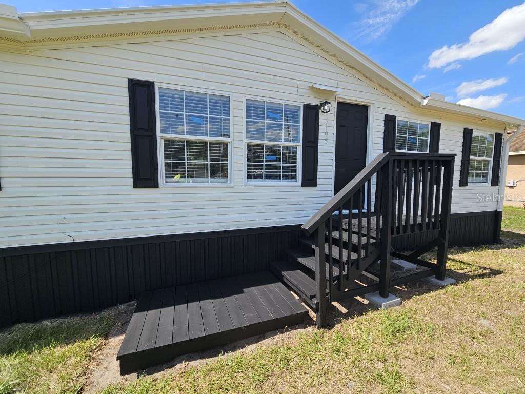 A manufactured home exterior features white siding, black shutters, and a black wooden porch — 5105 COUNTRYSIDE COURT, ST CLOUD, FL