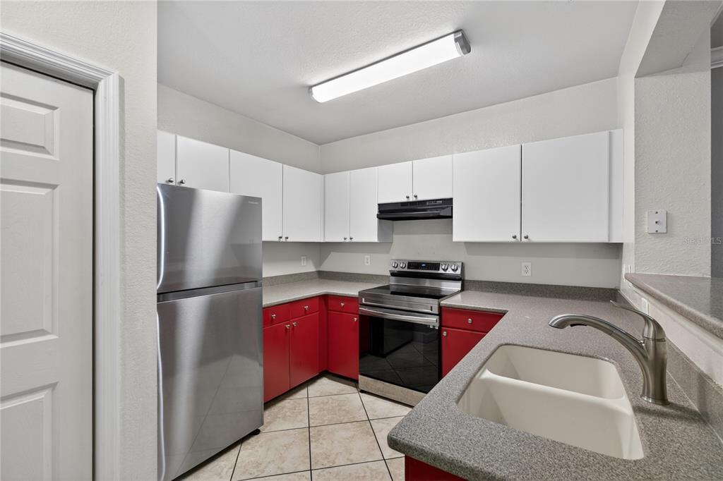 A kitchen features white upper cabinets, red lower cabinets, gray countertops, and stainless steel appliances — 300 E SOUTH STREET UNIT 2014, ORLANDO, FL