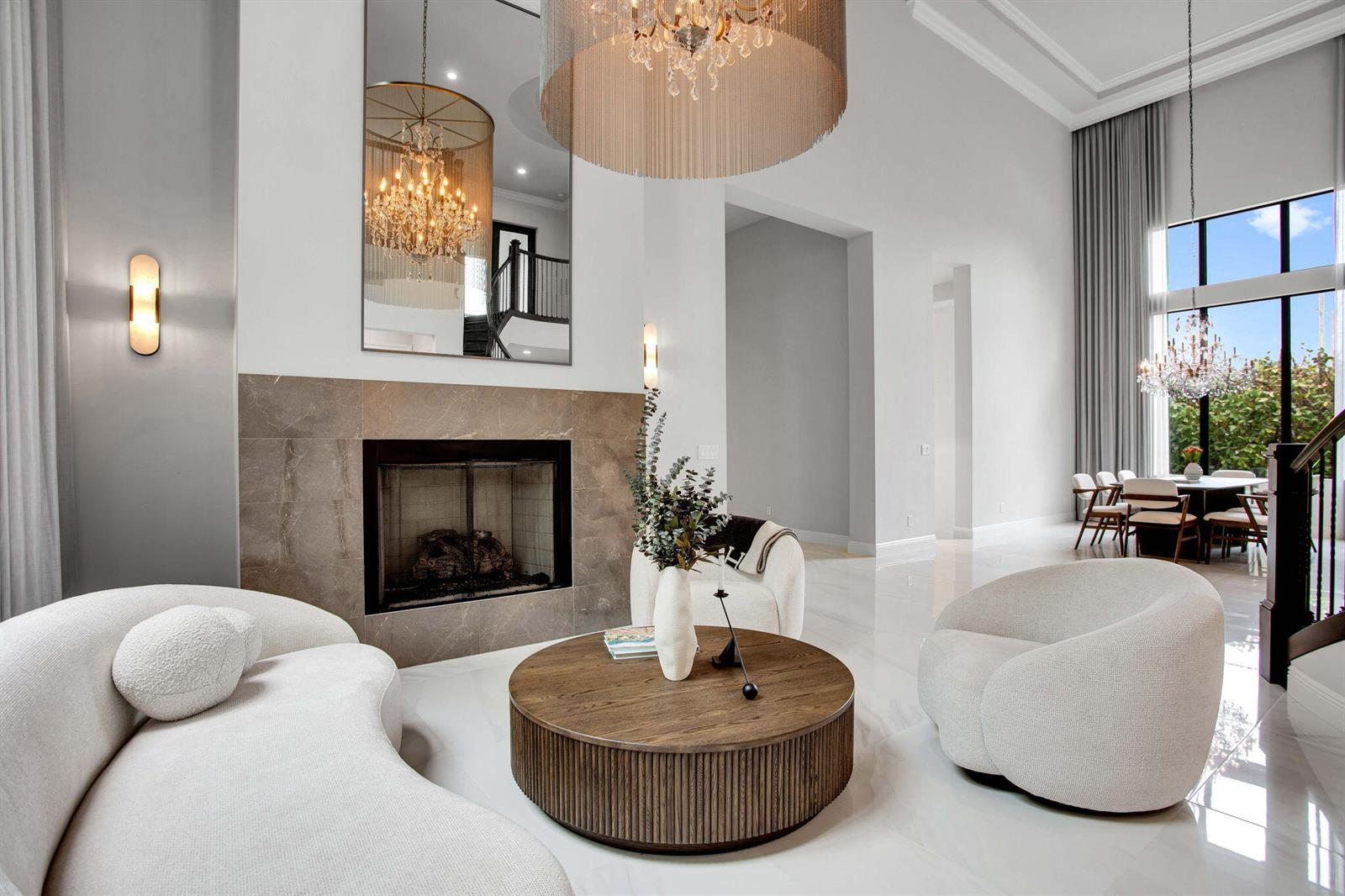 A modern living room features a fireplace, a round coffee table, and a large chandelier — 6903 NW 28th Avenue, Boca Raton FL 33496, BOCA RATON, FL