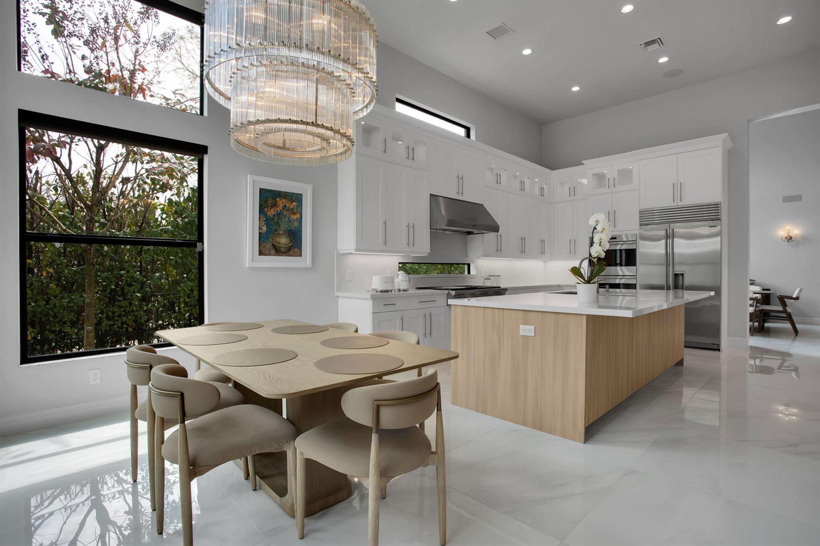 A modern kitchen and dining area features white cabinetry, a wood-toned island, and a crystal chandelier — 6903 NW 28th Avenue, Boca Raton FL 33496, BOCA RATON, FL