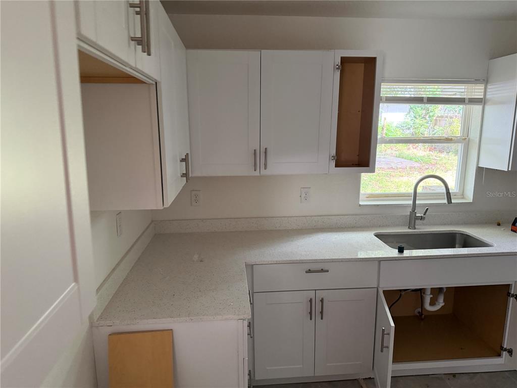 A kitchen features white shaker cabinets, light speckled countertops, and an undermount stainless steel sink — 6 S BARBOUR STREET, BEVERLY HILLS, FL
