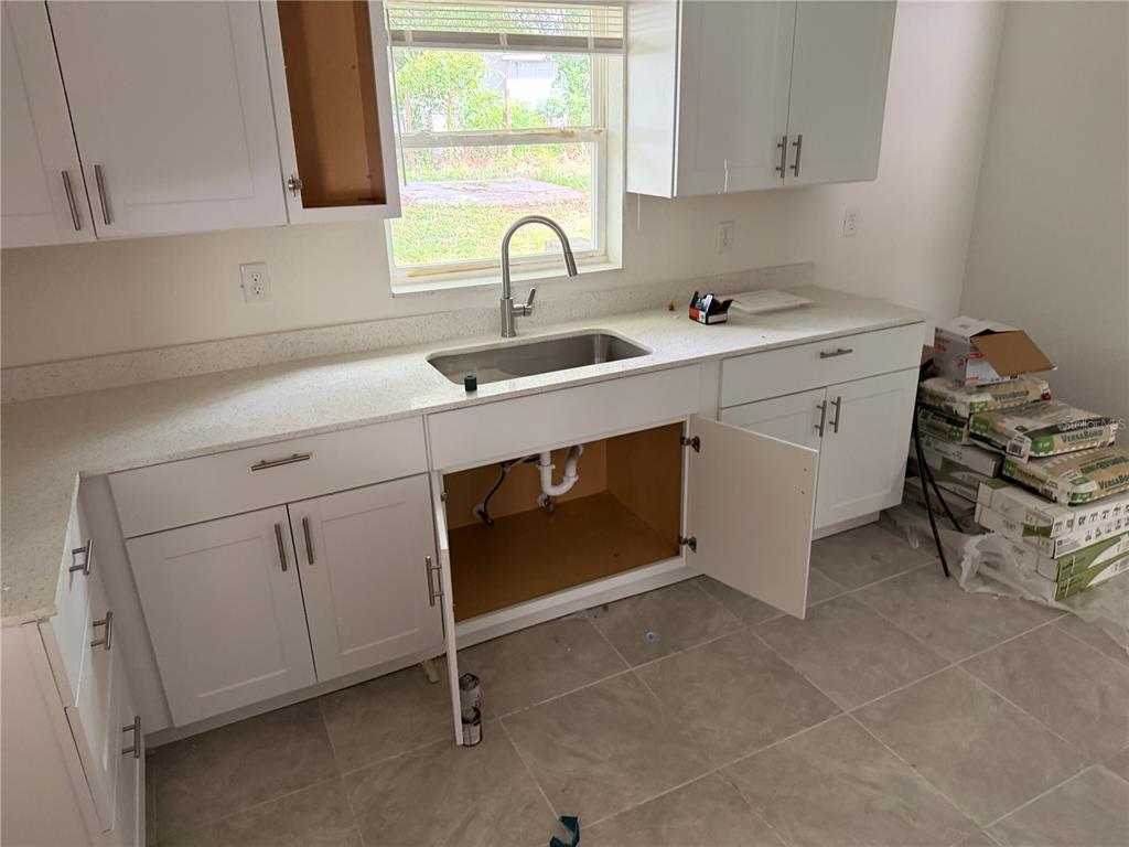 A kitchen features white cabinets, light countertops, a stainless steel sink, and tile flooring — 6 S BARBOUR STREET, BEVERLY HILLS, FL