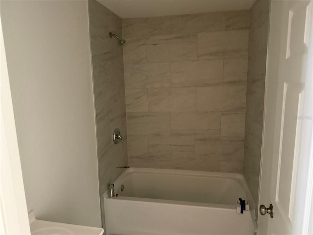 A bathroom features a white bathtub with light-colored, horizontal rectangular wall tiles — 6 S BARBOUR STREET, BEVERLY HILLS, FL