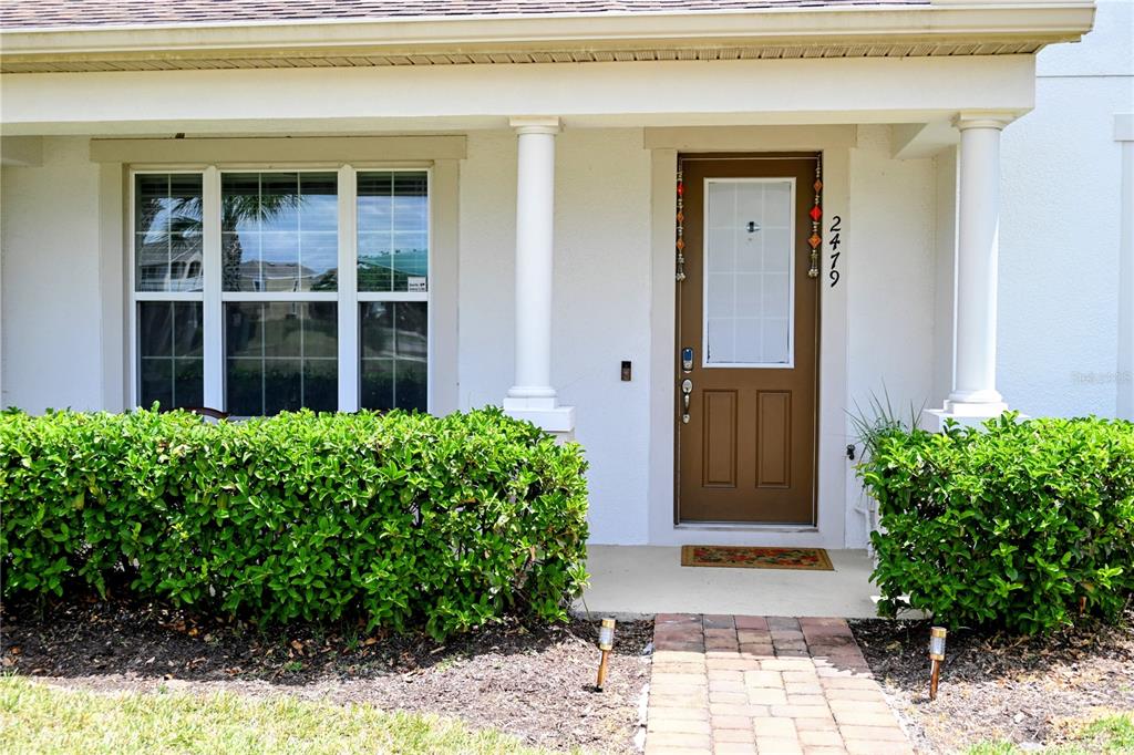 A brown front door with a glass pane sits between two white columns on a porch — 2479 TOSCOLONA DRIVE, KISSIMMEE, FL