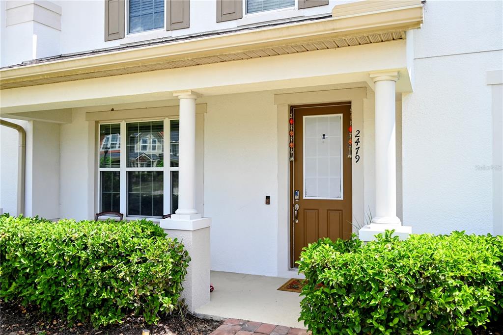 A front porch with white columns, a brown door, and green bushes in front — 2479 TOSCOLONA DRIVE, KISSIMMEE, FL