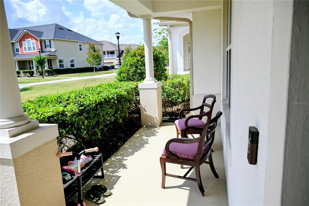 A covered front porch features two wooden chairs with purple cushions and a shoe rack — 2479 TOSCOLONA DRIVE, KISSIMMEE, FL