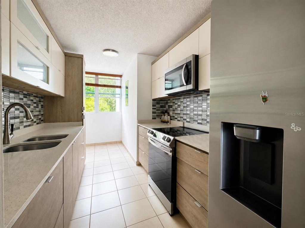 A galley kitchen features light wood cabinets, stainless steel appliances, and a tiled backsplash — CARR 844 1D-5 SAN JUAN CHALETS APT. 8050, SAN JUAN, PR